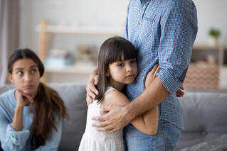 Small child hugging her father with mother looking on at them both. Attachment issues and trauma as a child can have adverse effects if not treated. Get help in Ewing, NJ at Mindful and Multicultural Counseling